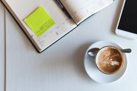 Coffee cup by mobile phone and diary on table