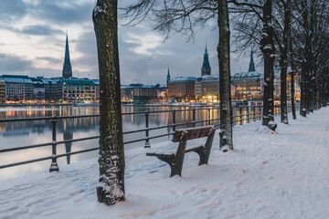 Germany, Hamburg, Illuminated city architecture reflecting in Binnenalster lake at dusk in winter
