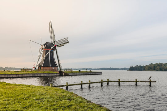 Netherlands, Groningen, Groyne in front of riverside windmill at dusk