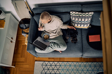 Smiling trendy senior woman with short hair sitting on the sofa with her dog and using technologies.