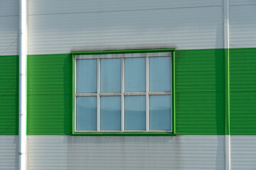 Fototapeta premium a window in the wall of a modern factory or a large shopping center. Details of the aluminum facade of an industrial building. The building is made of corrugated aluminum plates of green and white
