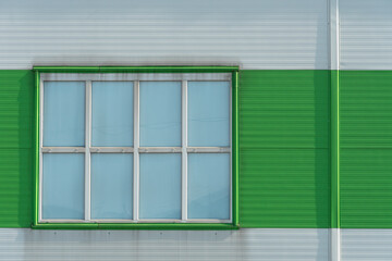 a window in the wall of a modern factory or a large shopping center. Details of the aluminum facade of an industrial building. The building is made of corrugated aluminum plates of green and white