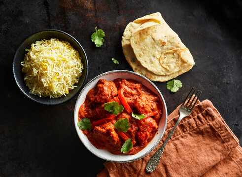 Studio shot of bowl of chicken tikka, bowl of basmati rice and naan bread