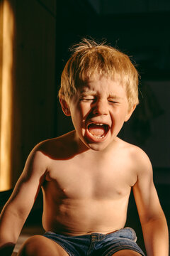 Displeased boy screaming while sitting on floor during dusk at home