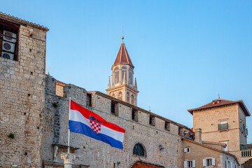 Croatia, Split-Dalmatia County, Trogir, Croatian flag hanging in front of old town houses with bell tower of Church of Saint Nicholas in background