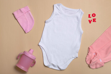 Close-up top view. Mockup blank pink bodysuit, pink pants, hat and cup for newborns on a beige...