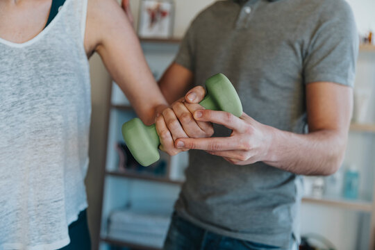 Physiotherapist with dumbbell guiding female patient in exercising in medical practice