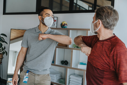 Mature male patient doing elbow bump with physiotherapist during pandemic