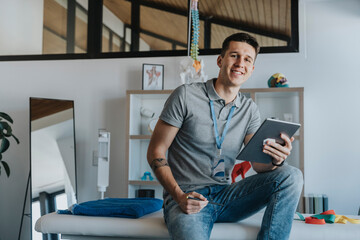 Smiling male physiotherapist with digital tablet sitting on bed in medical practice