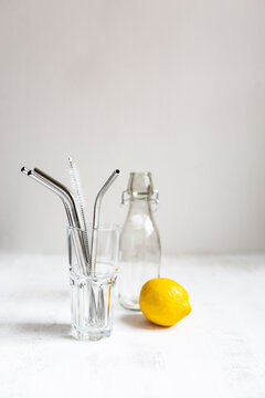 Reusable stainless steel drinking straws by glass and lemon on white background
