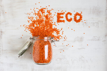 Eco text arranged with orange lentil by open jar on white background