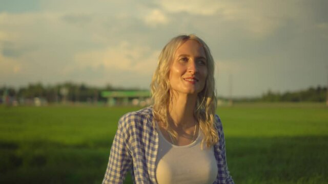 Beautiful young blonde woman with wavy hair in jeans, shirt, shirt stands in a field rejoicing. Girl smiles and laughs, she is happy. Summer day in the field