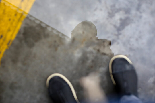 Chão de fábrica, sapatos preto e branco, no reflexo a silhueta da fotógrafa usando capacete de segurança