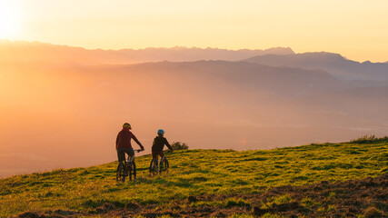 Mother and daughter cycling downhill with mtb bikes at a sunset.