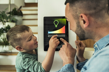 Boy adjusting lights on digital tablet with father at smart home