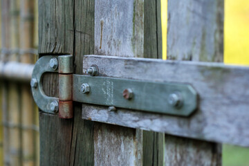 dobradiça em metal, presa a um portão rústico de madeira ressecada pelo tempo