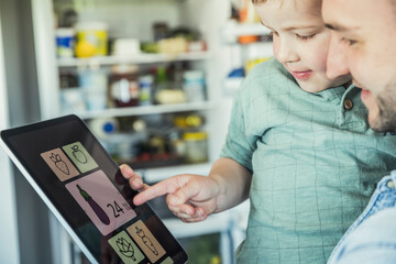 Smiling father carrying son pointing at digital tablet