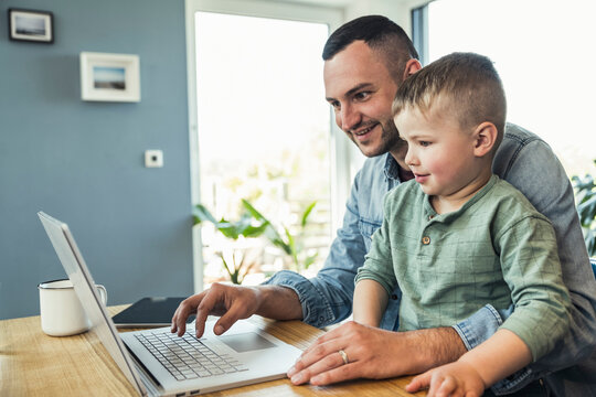 Smiling male freelancer using laptop while sitting with son at home