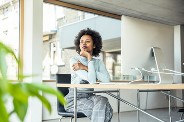 Female entrepreneur with hand on chin contemplating while sitting at desk in office