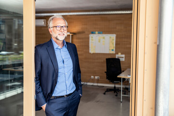 Mature businessman looking away while leaning on doorframe at office