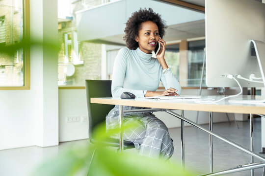 Businesswoman Talking On Mobile Phone While Working On Computer At Office