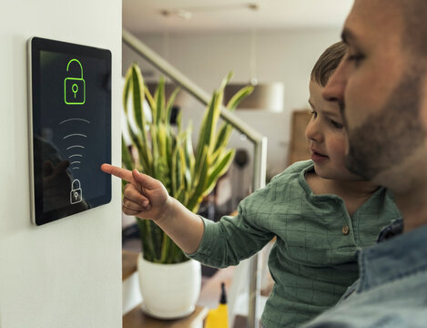 Father carrying son pointing at security tablet in smart home