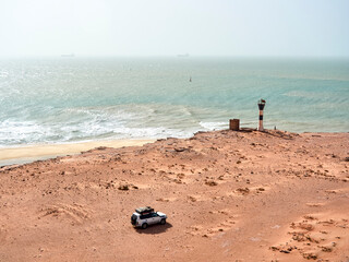Off-road vehicle driving toward lifeguard hut overlooking sandy coastal beach