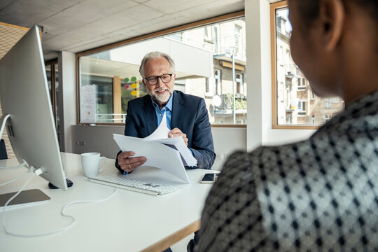 Smiling male professional reading documents in front of computer at office