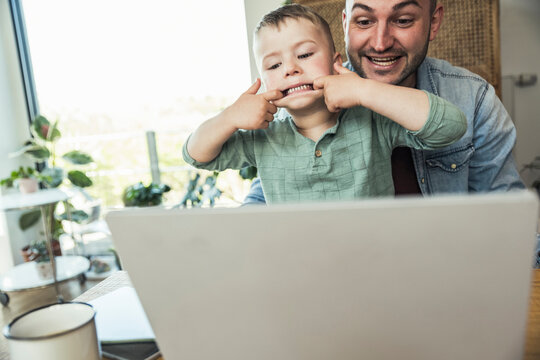 Boy teasing while sitting with father doing video call through laptop at home