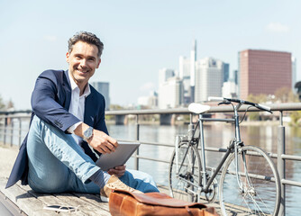 Mature businessman with digital tablet sitting by bicycle during sunny day