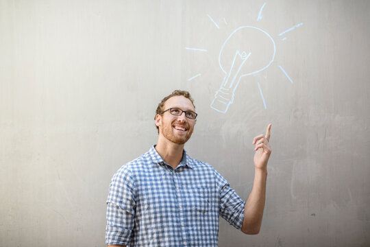 Man standing next to a wall with a lightbulb chalk drawing