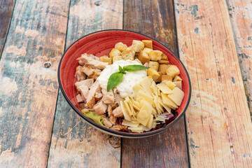 Amazing caesar salad with lots of flaked parmesan cheese, chicken pieces, mayonnaise and croutons inside a red bowl