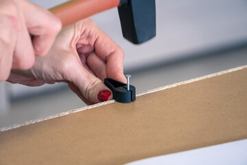 Close-up of Woman hammers by mallet hammer of steel nail into furniture during assembling manual furniture. Moving in new house