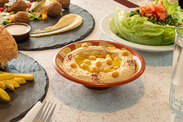 Table with various Arabic dishes and the center a clay bowl with chickpea hummus