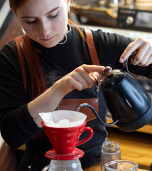 Barista pouring boiling water of manual drip brewer and make coffee. Girl pouring on coffee ground with filter. Alternative pure over method.