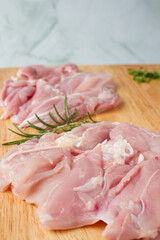 Raw chicken breast with herbs over a wood plate, green background