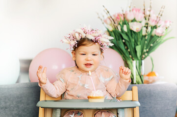 Adorable baby girl sitting in a chair, looking at cupcake with one candle, first birthday party