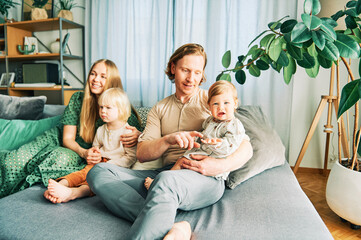 Happy young family of four relaxing on a couch, couple playing with baby girl and toddler boy