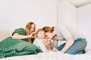Obraz na płótnie Canvas Young happy couple mother and father playing with adorable toddler 1 year old girl, family relaxing in bed