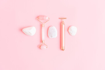 Obraz na płótnie Canvas top view of quartz and metal face massagers with white stones copper pink background. skin care concept. personal care. flat lay