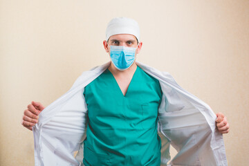 Fototapeta na wymiar Doctor in protective medical mask and green suit opens his white coat isolated