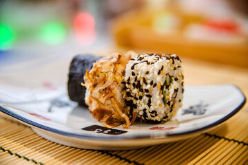 Several sushi on a white plate standing on a bamboo tablecloth
