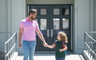 Parent taking child to school. Pupil of primary school go study with backpack outdoors. Father and son run with father after come back from school. School, family, education and outdoor concept.