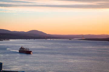 Obraz premium A freight ship navigating through St-Lawrence river at sunrise, with majestic landscape in background, Quebec city harbor, Canada