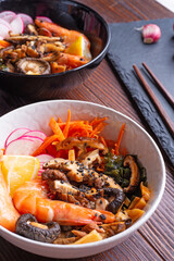 miso soup with mussels, shrimps , shiitake mushrooms and vegatables. served at dark brown wooden table. flat lay