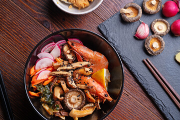 miso soup with mussels, shrimps , shiitake mushrooms and vegatables. served at dark brown wooden table. flat lay