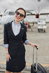 Stewardess with baggage on runway near airplane