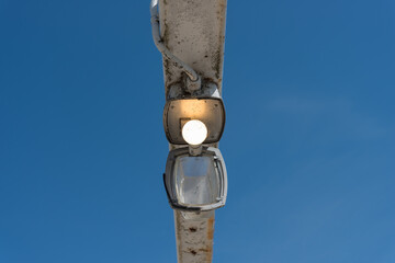 old walkway lamp with diffuser glass cover hanging down and illuminated LED bulb against a blue sky