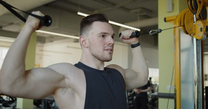 Young attractive muscular athlete works out in a modern gym. Strong man doing overhead cable curl exercise during training. Active healthy lifestyle and wellbeing.