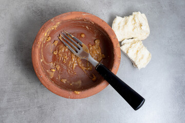 Empty clay pot with food scraps, a metal fork with a black handle and bread scraps. After the meal.
